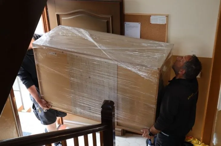 zwei umzugshelfer tragen grossen schrank im treppenhaus